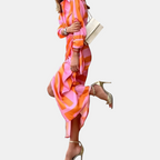 Walking view of the Freya Summer Midi Dress Striped Wrap in orange, showcasing the flowing midi-length skirt, wrap waist tie, and vibrant striped design in motion. Designed by Bella Hudson.