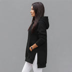 Side view of the Wilhelmine oversized side-slit hoodie in black, showcasing its relaxed silhouette, long sleeves, cozy hood, and side-slit detailing.