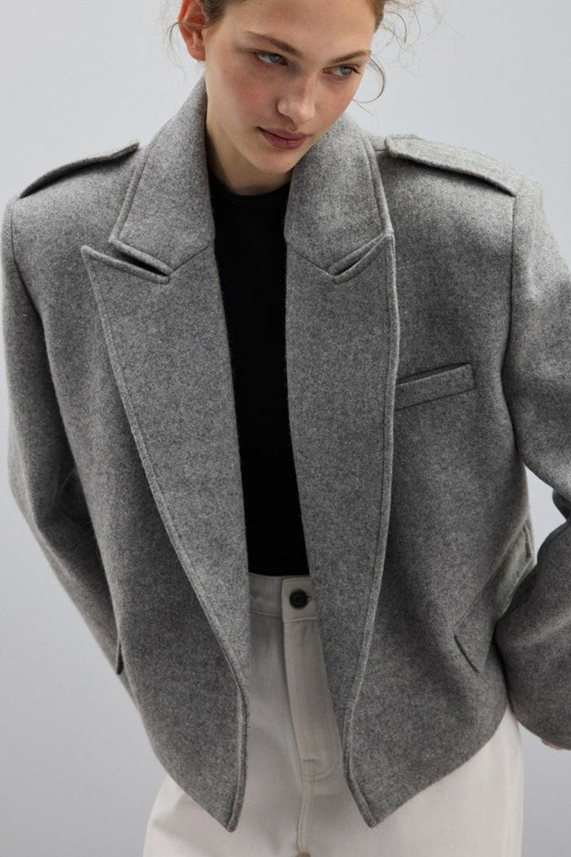 Adele Gray short jacket with wide notched lapels and shoulder epaulettes over a black top.
