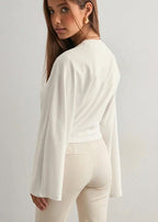 Alina White top seen from the back with long flared sleeves, styled with beige tailored pants.