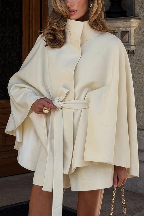 Amalia Beige cape coat with high collar and tied belt styled with matching shorts, shown in a close front view.