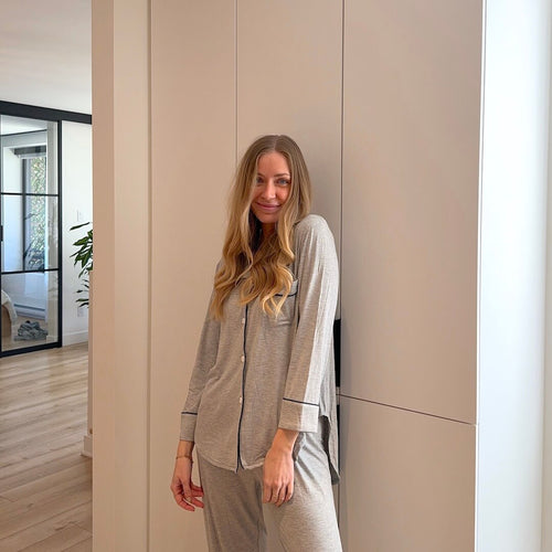 Ana Gray pajama set with a button-up top and contrast piping worn by a model leaning against a wall.