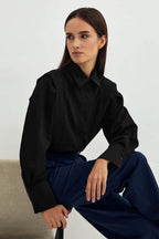 Ariana Black button-down shirt worn seated with navy wide-leg trousers, showing the point collar and buttoned cuffs.