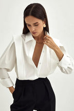 Ariana White button-down shirt worn open at the neckline with black trousers, showing the pleated shoulder detail.