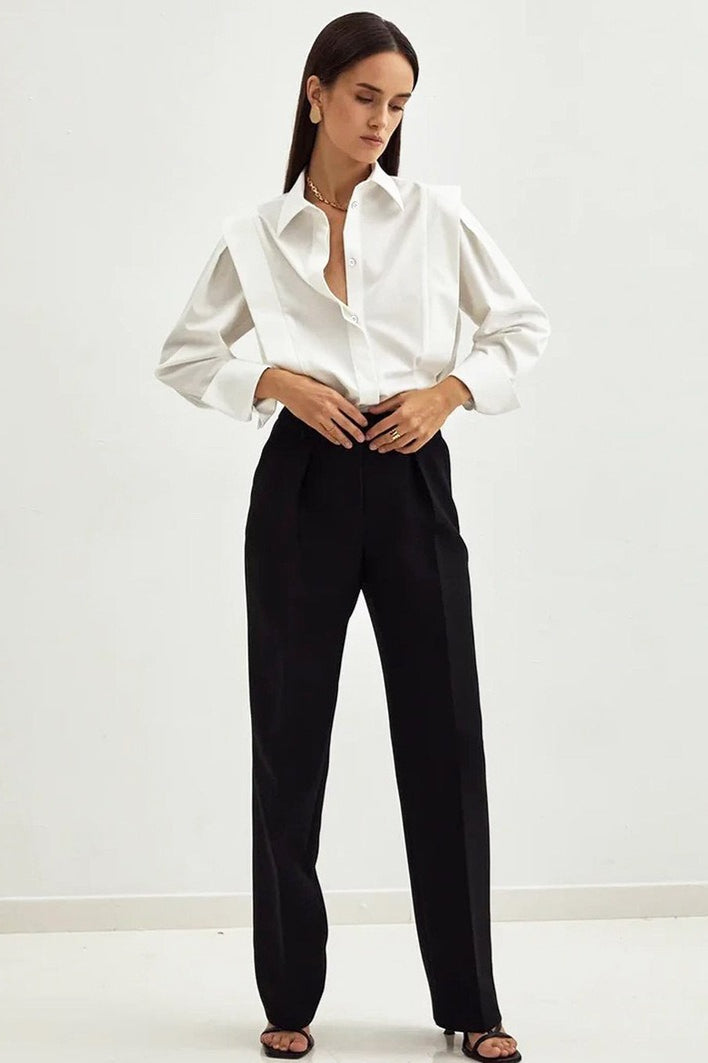 Ariana White button-down shirt in a full-body look with black pleated trousers and strappy sandals.
