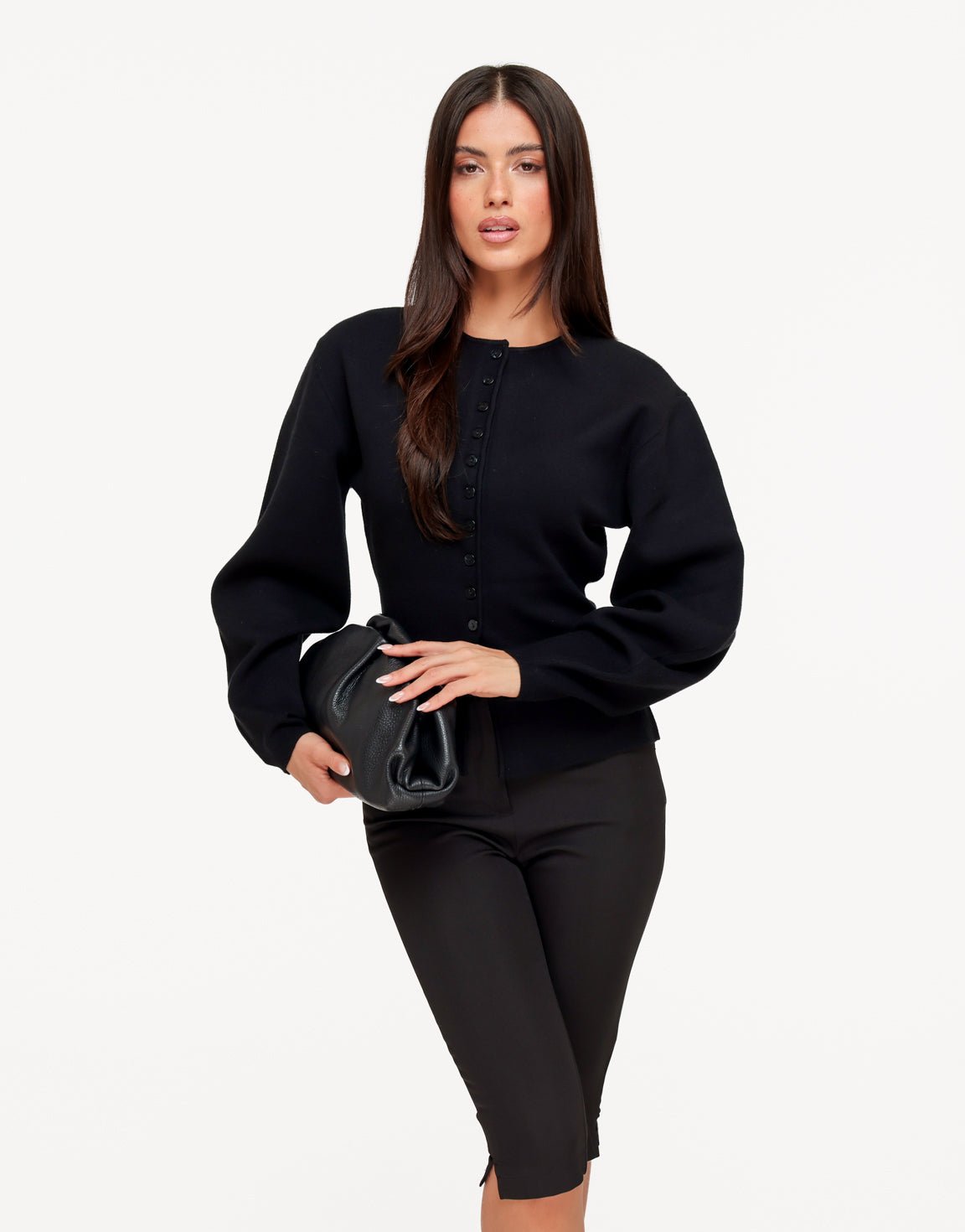 Aurelia Black cardigan with cinched waist and peplum hem styled with black pants while holding a clutch.
