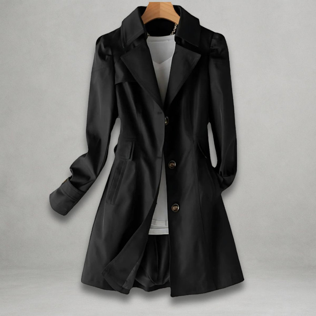 Front view of the Aurora Trench Coat with Belted Notch Collar in black, featuring wide notched lapels, a button-front closure, long sleeves with cuff straps, matching waist belt, and a flared mid-length silhouette. Designed by Bella Hudson.