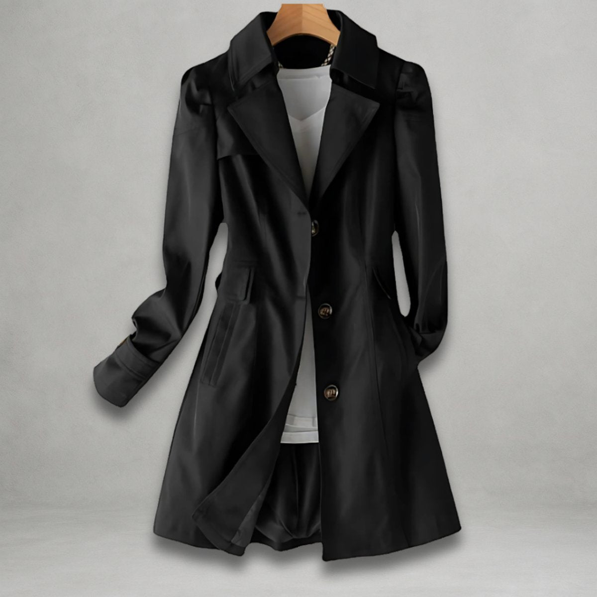 Front view of the Aurora Trench Coat with Belted Notch Collar in black, featuring wide notched lapels, a button-front closure, long sleeves with cuff straps, matching waist belt, and a flared mid-length silhouette. Designed by Bella Hudson.