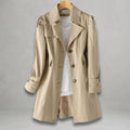 Front view of the Aurora Trench Coat with Belted Notch Collar in khaki, featuring wide notched lapels, a button-front closure, long sleeves with cuff straps, matching waist belt, and a flared mid-length silhouette. Designed by Bella Hudson.