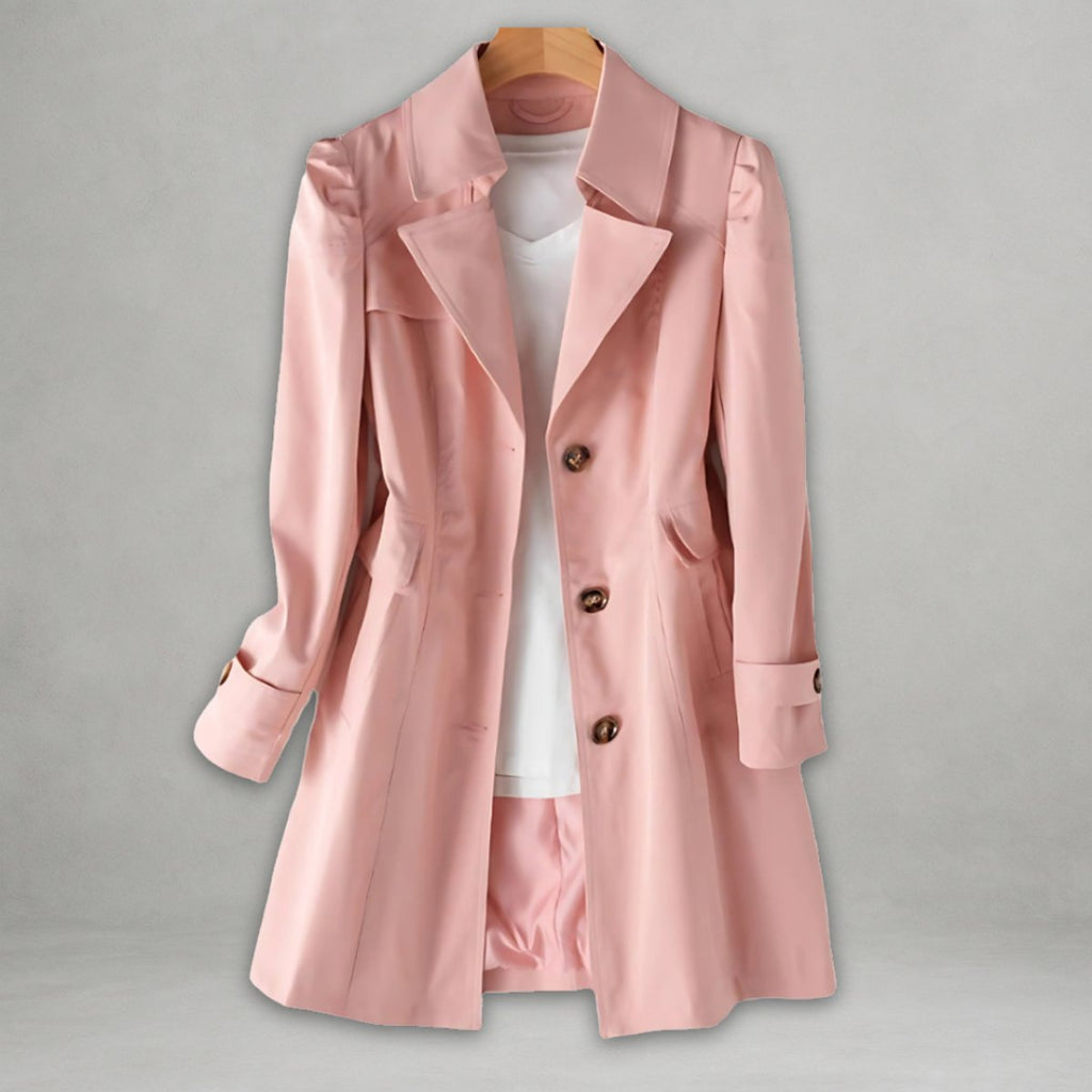 Front view of the Aurora Trench Coat with Belted Notch Collar in pink, featuring wide notched lapels, a double-breasted button front, long sleeves with cuff straps, matching waist belt, and a flared mid-length silhouette. Designed by Bella Hudson.