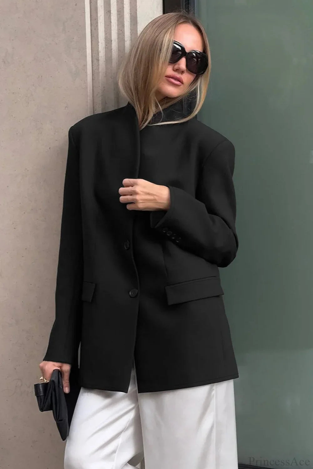 Aveline Black stand collar blazer with two-button front and flap pockets, styled with white trousers.