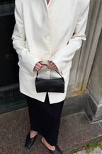 Aveline White blazer close-up of the button front and long sleeves with a black bag.