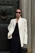 Aveline White stand collar blazer worn open over a black dress in front of a dark ornate door.