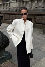 Aveline White blazer with a hand in the pocket, styled with a black maxi dress.