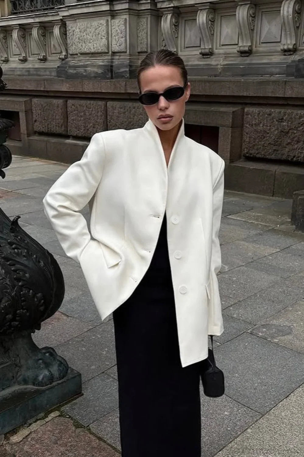 Aveline White blazer with a hand in the pocket, styled with a black maxi dress.