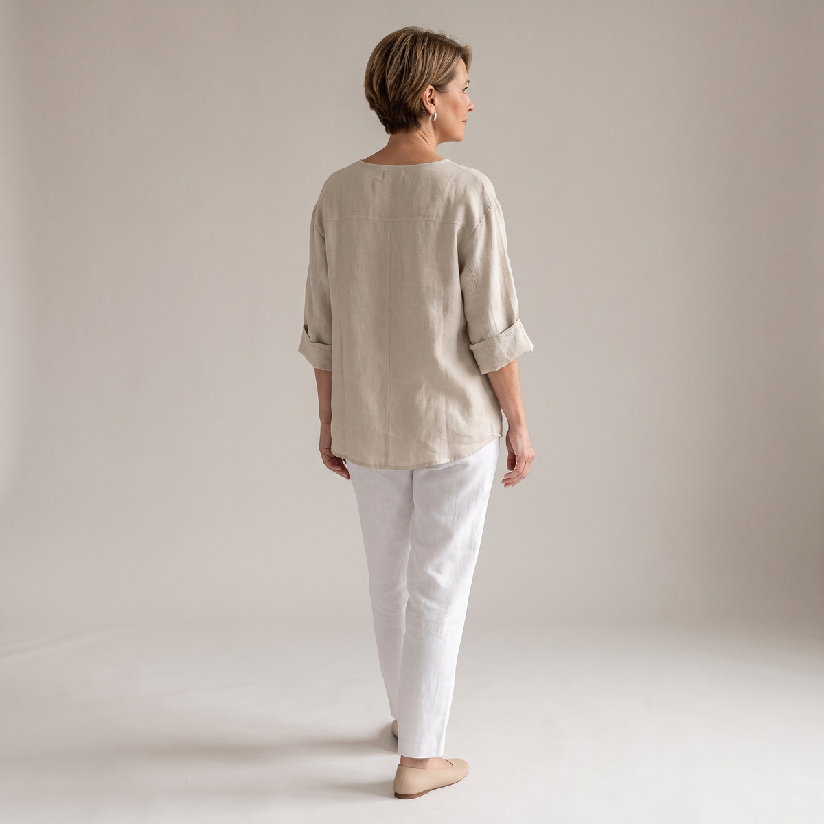 Back view of the Averil Blouse Linen Long-Sleeve in beige, highlighting the relaxed silhouette, long rolled sleeves, and lightweight linen construction. Designed by Bella Hudson.