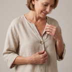 Close-up detail of the Averil Blouse Linen Long-Sleeve in beige, featuring the split V-neckline, decorative button detail, and textured linen fabric. Designed by Bella Hudson.