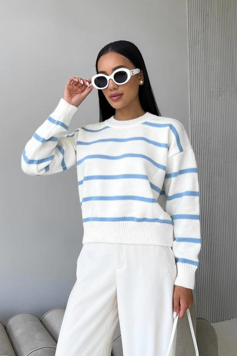 Avery Blue striped crew-neck sweater in white with light blue stripes worn with white trousers.