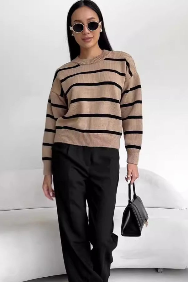 Avery Brown striped crew-neck sweater in tan with black stripes styled with black trousers and a handbag.