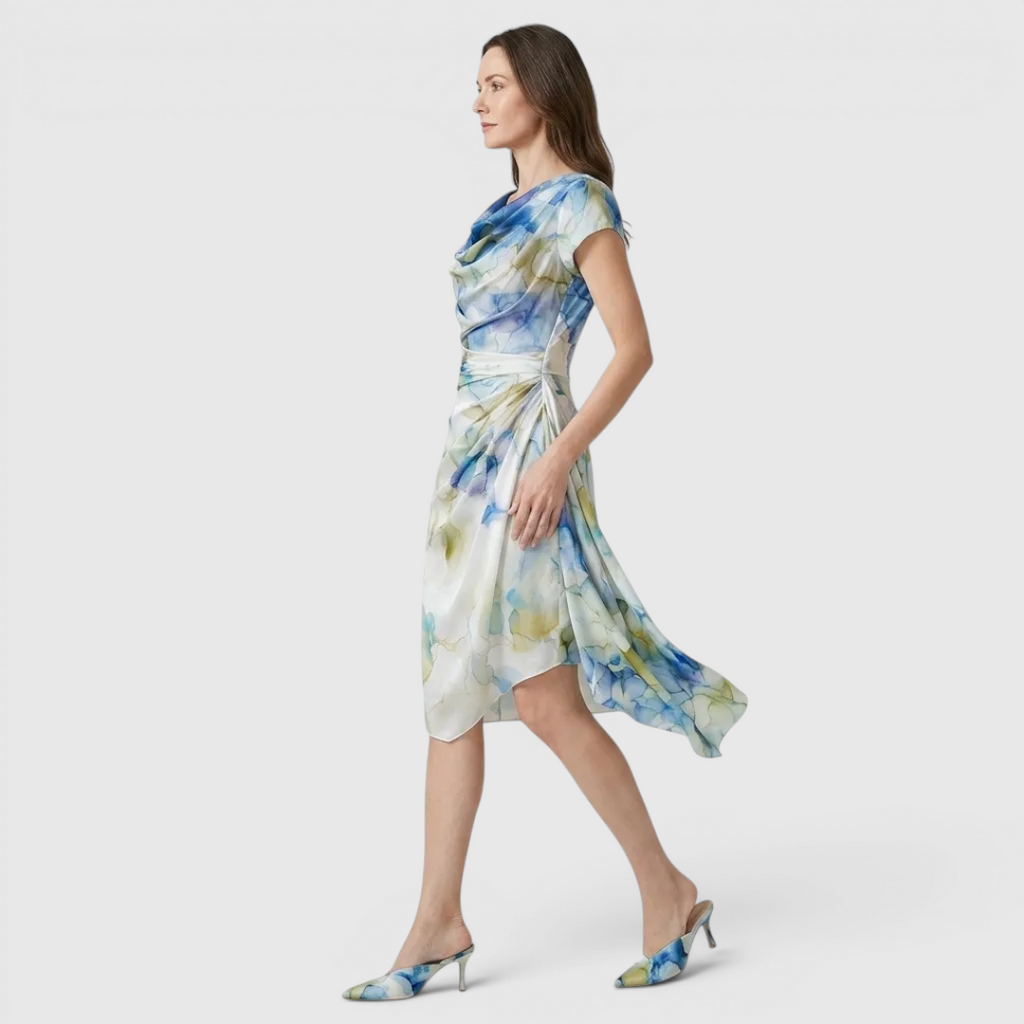 Side view of the Bianca Midi Lightweight Dress Watercolor-Print Cowl-Neck in sky blue, showcasing the draped cowl neckline, cap sleeves, flowing asymmetrical hem, and soft watercolor print. Designed by Bella Hudson.