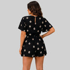 Back view of black floral romper with short sleeves and tie waist detail by BELLA HUDSON