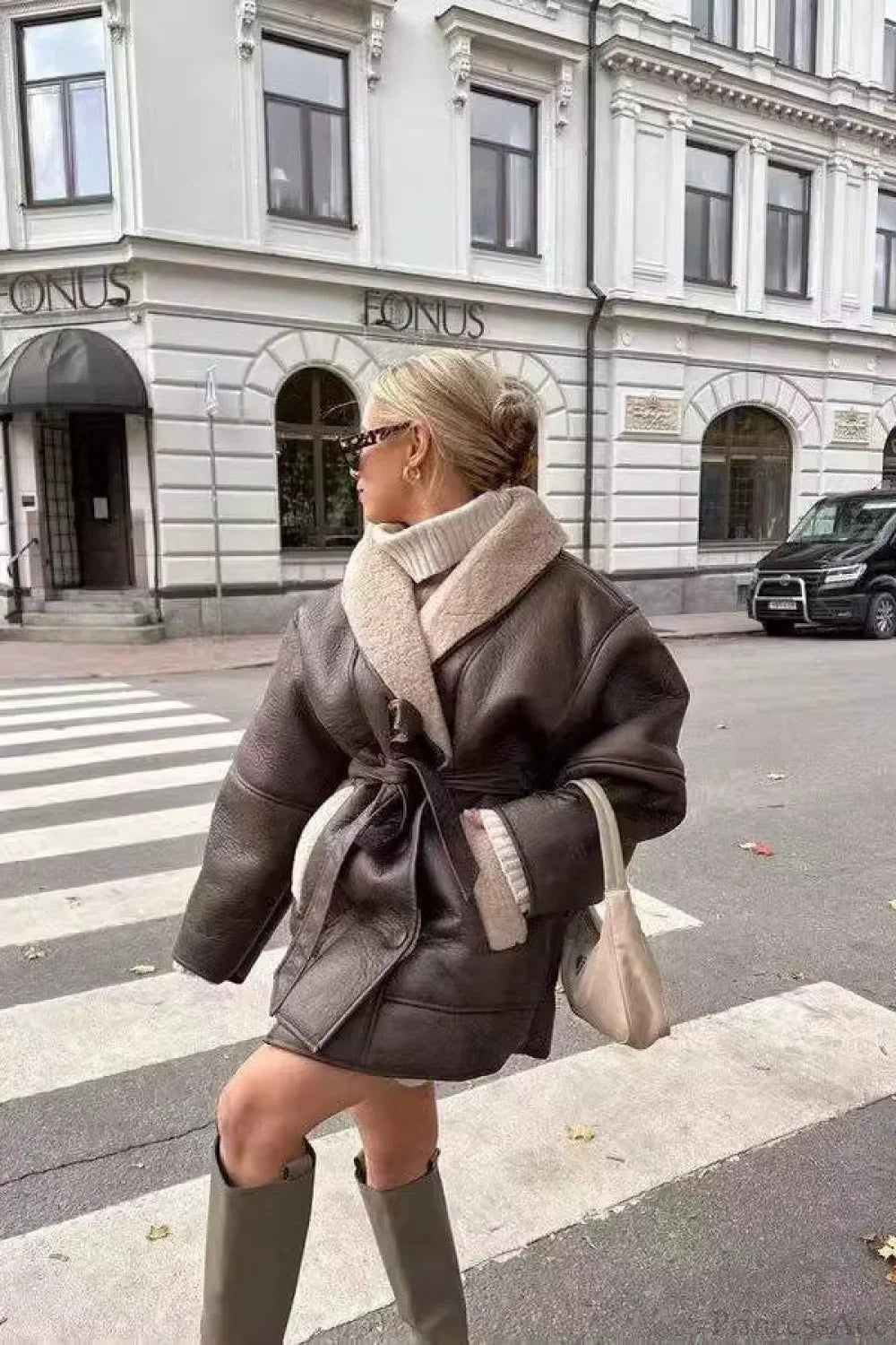 Brielle Brown faux leather belted jacket styled with a cream faux shearling collar, belted waist, and olive knee-high boots on a city crosswalk.