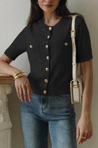 Clara Black short-sleeve knit cardigan with gold buttons and patch pockets, styled with jeans and a cream shoulder bag.