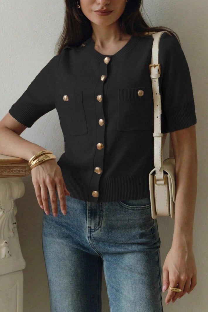Clara Black short-sleeve knit cardigan with gold buttons and patch pockets, styled with jeans and a cream shoulder bag.