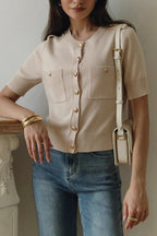 Clara Khaki short-sleeve knit cardigan with gold buttons and patch pockets, styled with blue jeans and a cream shoulder bag.