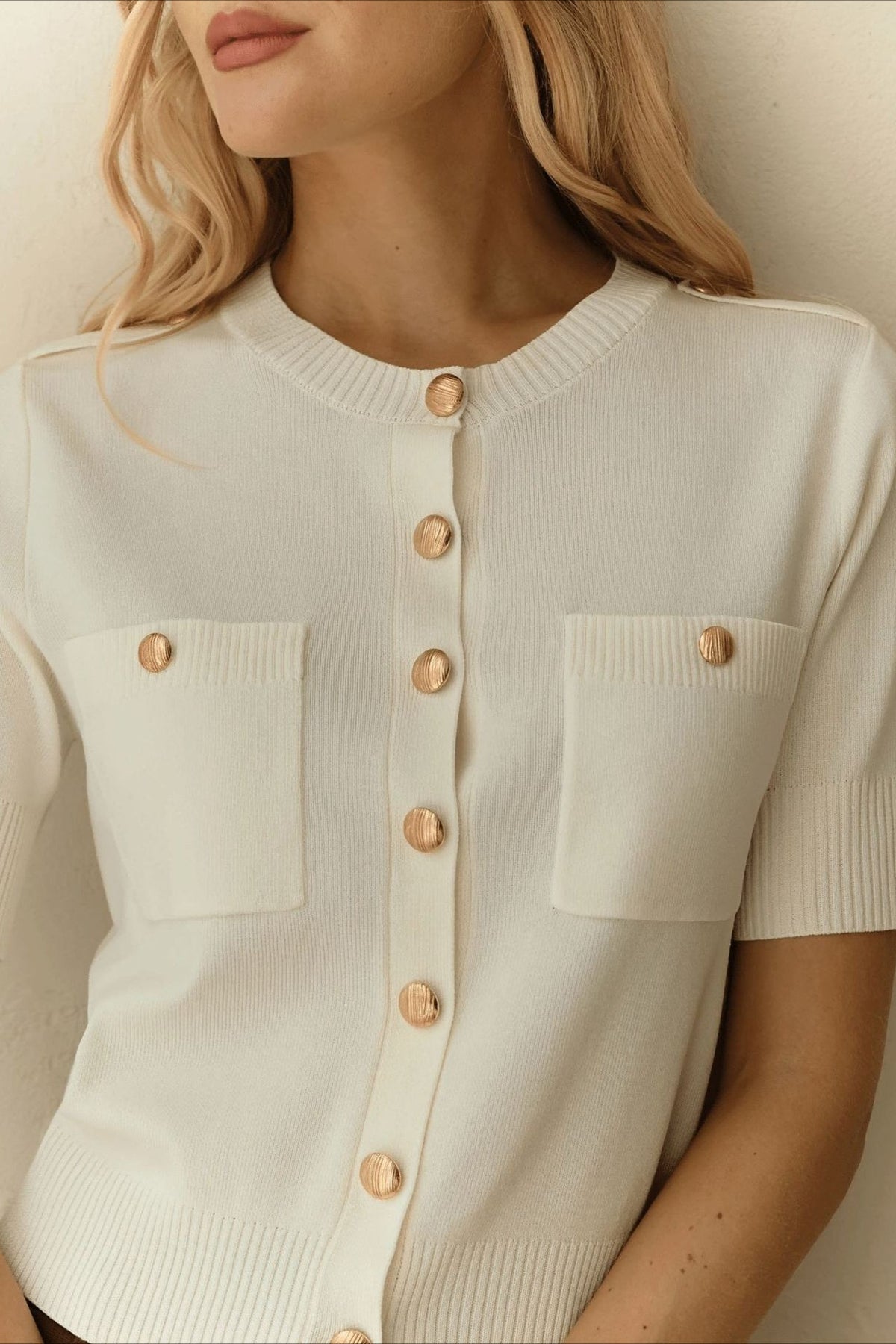 Clara White knit cardigan close-up of the round ribbed neckline, gold buttons, and patch pockets.