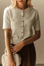 Clara White short-sleeve knit cardigan with gold buttons and patch pockets, styled with brown trousers and a quilted white bag.