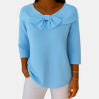 Front view of the Colette Bow-Tie Long Sleeve T-shirt in blue, featuring a decorative bow neckline, ribbed knit texture, three-quarter sleeves, and a relaxed curved hem. Designed by Bella Hudson.