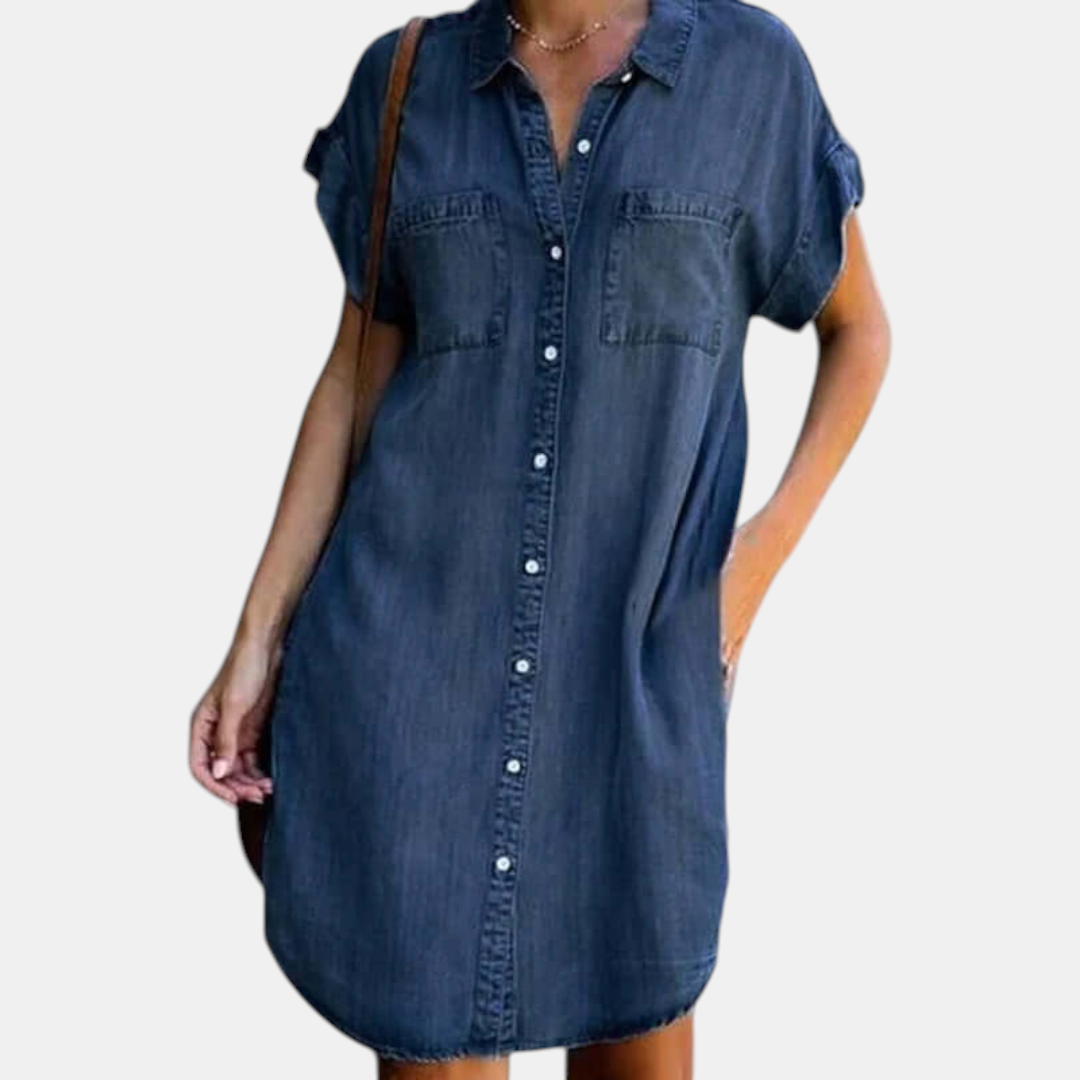 Front view of the Corinne Shirt Dress Chambray Denim Button-Front in dark blue, featuring a collared neckline, button-front closure, rolled cap sleeves, chest pockets, and a relaxed chambray silhouette. Designed by Bella Hudson.