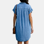 Back view of the Corinne Shirt Dress Chambray Denim Button-Front in light blue, highlighting the relaxed silhouette, back yoke detail, rolled cap sleeves, and soft chambray fabric. Designed by Bella Hudson.