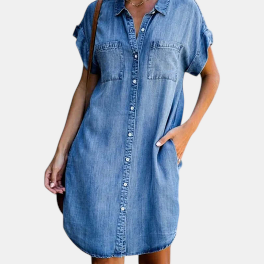 Front detail view of the Corinne Shirt Dress Chambray Denim Button-Front in light blue, showcasing the collared neckline, chest pockets, rolled cap sleeves, and relaxed shirt dress silhouette. Designed by Bella Hudson.