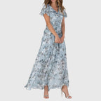 Front view of the Delphine Summer Maxi Dress Floral Print Flutter Sleeve in blue, featuring a V-neckline, flutter sleeves, floral print, and a flowing tiered maxi silhouette. Designed by Bella Hudson.