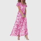 Front view of the Delphine Summer Maxi Dress Floral Print Flutter Sleeve in light pink, featuring a V-neckline, flutter sleeves, floral print, tiered skirt, and an elegant flowing silhouette. Designed by Bella Hudson.