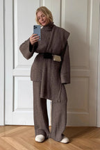 Elena Brown cable-knit turtleneck sweater, wide-leg pants, and scarf worn wrapped and belted at the waist.