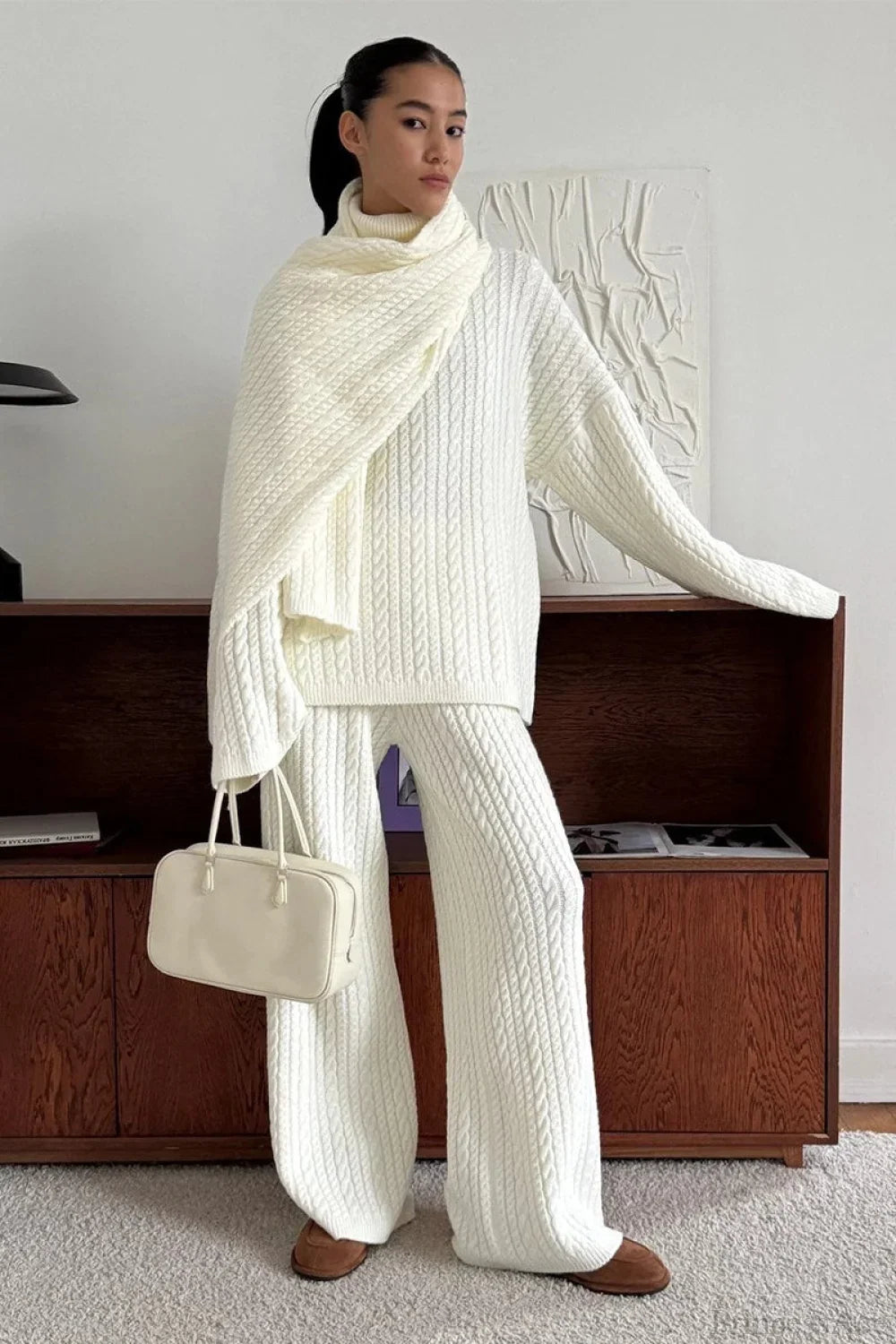 Elena White cable-knit turtleneck sweater with wide-leg pants and a draped matching scarf, styled with a cream handbag.