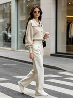 Elise Beige ribbed knit sweater styled full-body with cream wide-leg trousers and white sneakers on a city street.