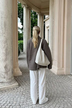 Elise Gray coat shown from the back with a short coat length and dropped shoulders, styled with white pants and a cream shoulder bag.