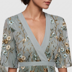 Close-up detail of the Elodie Summer Maxi Dress Floral Print Wide Sleeve in green, featuring the V-neck wrap neckline, wide flutter sleeves, floral print, and gathered waist detail. Designed by Bella Hudson.