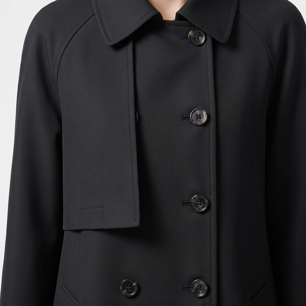 Close-up detail view of the Emilia Trench Coat Midi Double-Breasted in black, highlighting the pointed collar, double-breasted buttons, smooth fabric, and structured front construction. Designed by Bella Hudson.