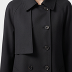 Close-up detail view of the Emilia Trench Coat Midi Double-Breasted in black, highlighting the pointed collar, double-breasted buttons, smooth fabric, and structured front construction. Designed by Bella Hudson.
