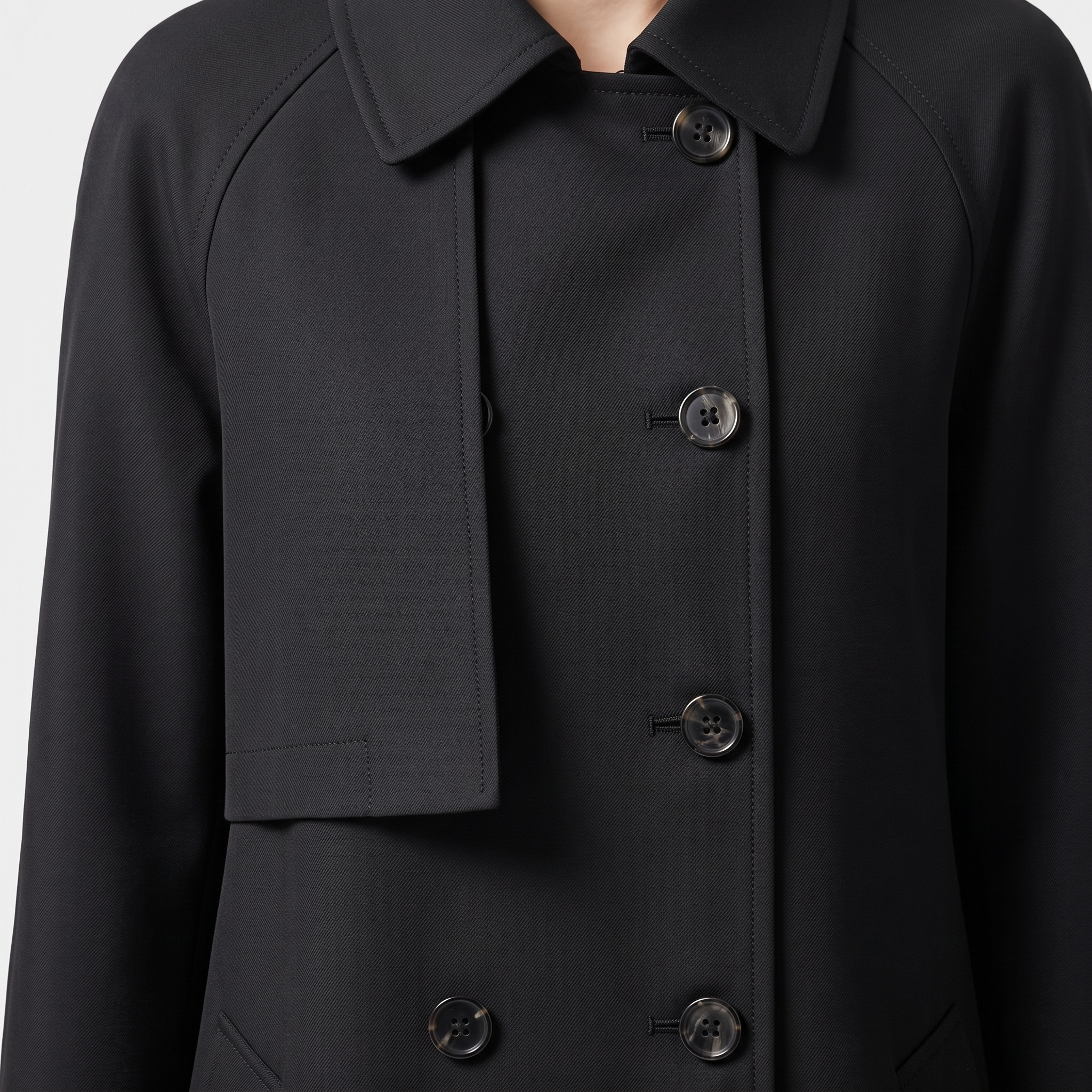 Close-up detail view of the Emilia Trench Coat Midi Double-Breasted in black, highlighting the pointed collar, double-breasted buttons, smooth fabric, and structured front construction. Designed by Bella Hudson.