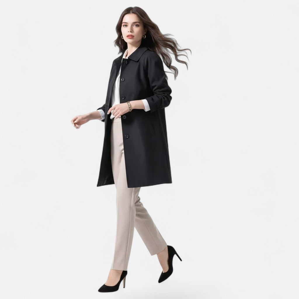 Front model view of the Emilia Trench Coat Midi Double-Breasted in black, showcasing the pointed collar, double-breasted button front, long sleeves, side pockets, and structured midi-length silhouette. Designed by Bella Hudson.