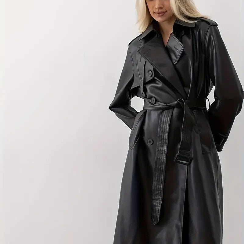 Front pose view of the Emma Trench Coat Faux-Leather Belted in black, featuring wide notched lapels, a tied waist belt, long sleeves, and a structured faux-leather silhouette. Designed by Bella Hudson.