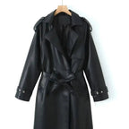 Front product view of the Emma Trench Coat Faux-Leather Belted in black, featuring wide notched lapels, a double-breasted button front, matching tie waist belt, long sleeves with cuff straps, and a knee-length faux-leather silhouette. Designed by Bella Hudson.