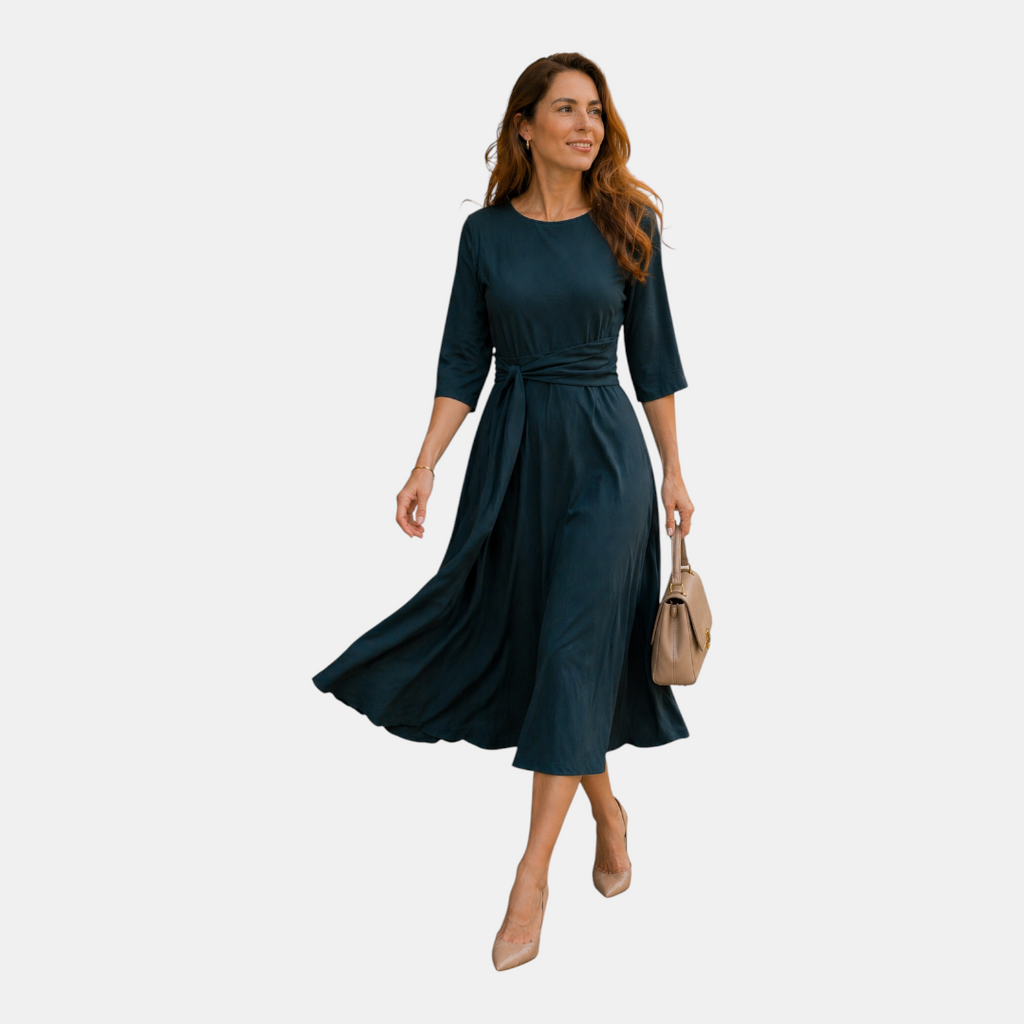 Walking view of the Estelle Midi Dress Cotton A-Line Tie-Waist in green, showcasing the flowing midi-length skirt, three-quarter sleeves, and adjustable tie waist. Designed by Bella Hudson.