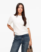 Estelle White short sleeve crewneck sweater shown from the front with one hand on the hip and wide-leg jeans.